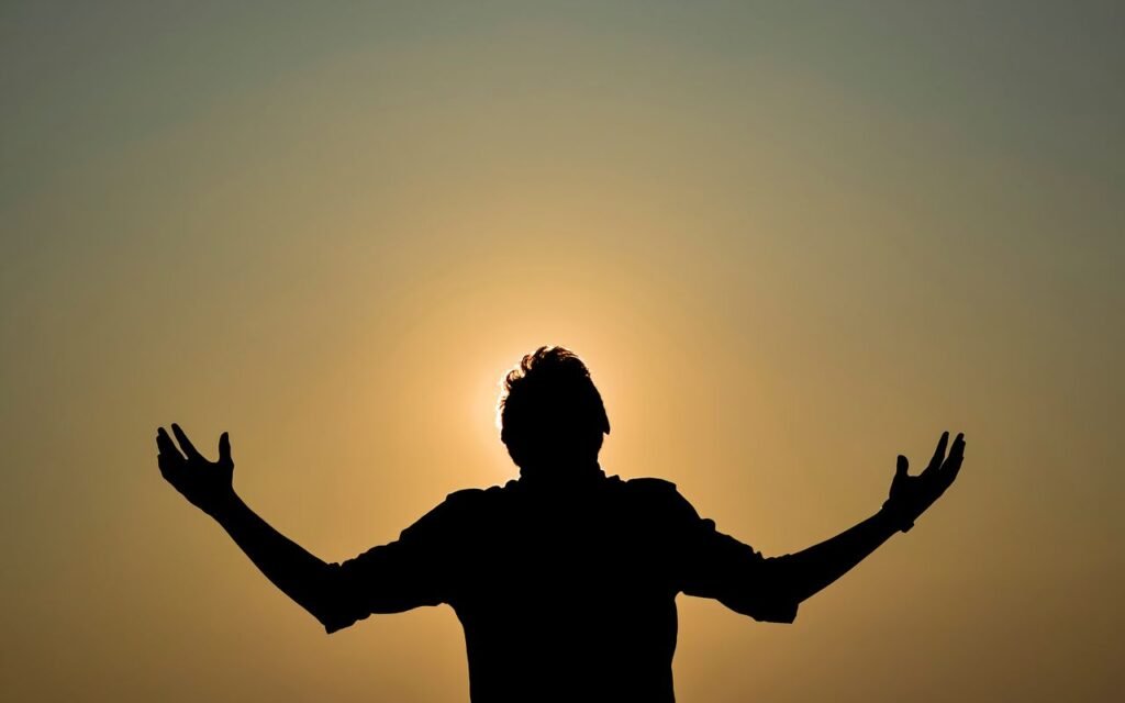 Captivating silhouette of a man with raised hands against a golden sky during sunset, capturing a dramatic moment.